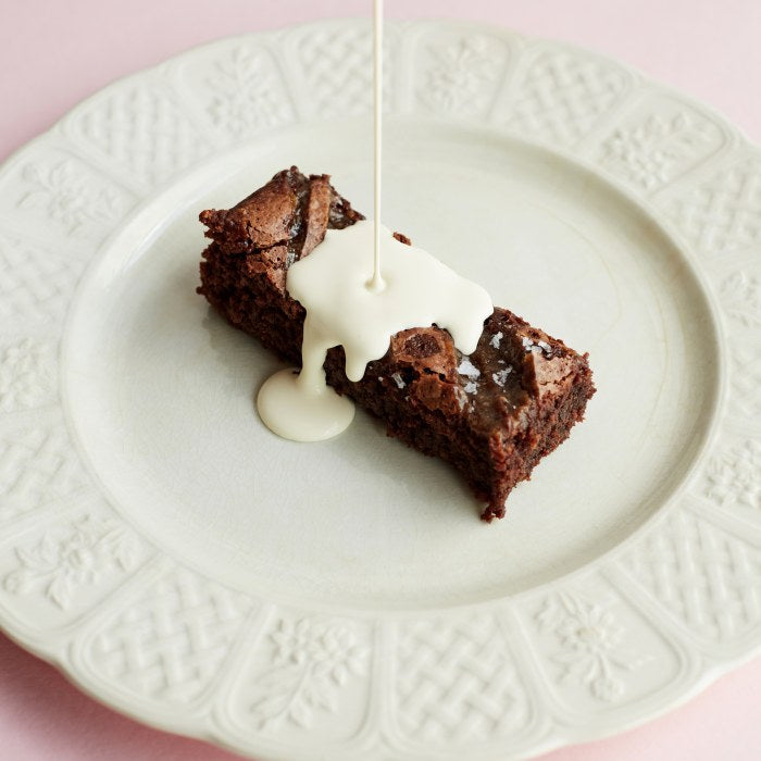 A single portion of Exploding Bakery Salted Caramel Brownie with cream bing poured over it.